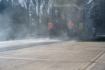 Construction workers in safety vests in the smoke behind an asphalt paving machine, road repaving...
