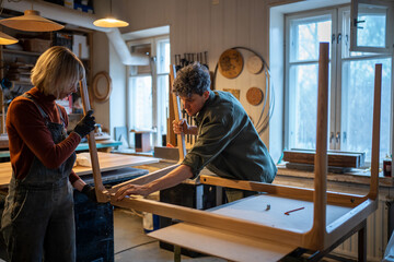 Carpentry workshop. Focused woman and man working in carpentry workshop assembling table, joining...