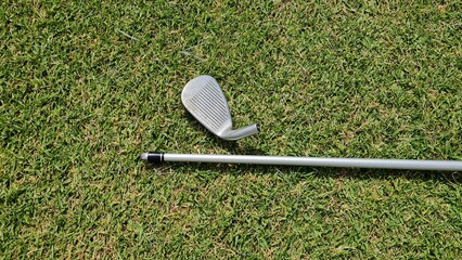 Broken golf club, top part lays on green grass 