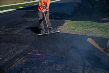 Construction worker with asphalt rake smoothing out fresh blacktop on driveway
