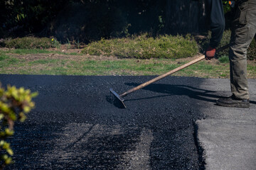 Construction worker with asphalt rake smoothing out fresh blacktop on driveway
