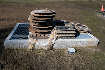 Fototapeta premium New community construction project, equipment vault in freshly seeded grass with iron collars and lids stored on top 