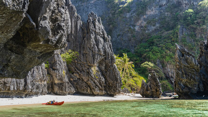 Picturesque karst rocks rise above the emerald water. Steep slopes, sharp peaks. The canoe is...