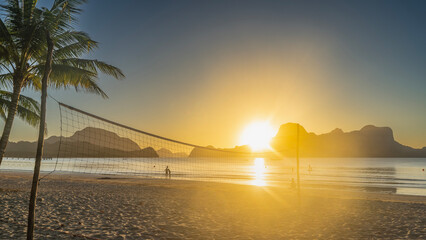 Sunset on a tropical beach. A volleyball net is stretched over the sand. The rays of the setting...