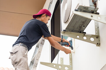 Technician man using a screwdriver to fix and install new air conditioner, repair service, and...