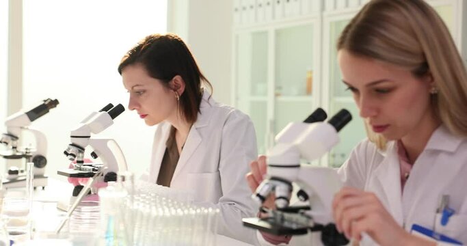 Young female researchers working together in a clinical laboratory examine a sample using a microscope