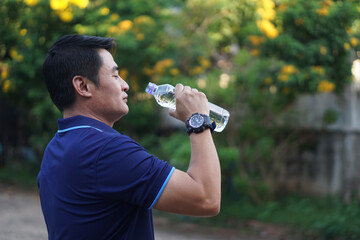Asian man holds bottle of drinking water to drink outdoor. Concept, Drink water for good health. Relief from thirsty, and protect from heat stroke, cool down in hot weather condition. Health care.