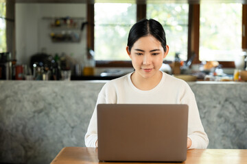 Young asian beautiful business woman working with laptop sitting at home. Smiling charming happy young female doing homework meeting conference with team at home.