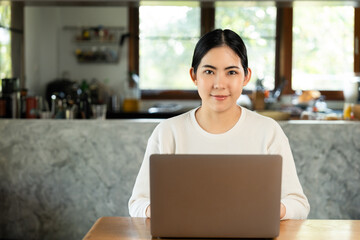 Young asian beautiful business woman working with laptop sitting at home. Smiling charming happy young female doing homework meeting conference with team at home.