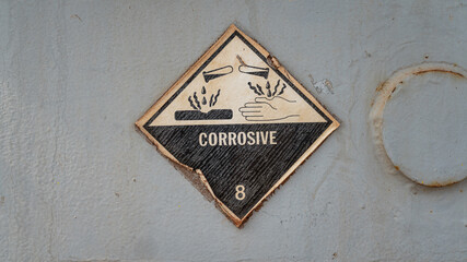 "Corrosive" hazardous material warning sign of the acid chemical which is showed on metal containment. Industrial safety sign. Close-up and selective focus.