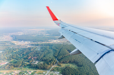 View of airplane wing, blue skies and green land during landing. Airplane window view.