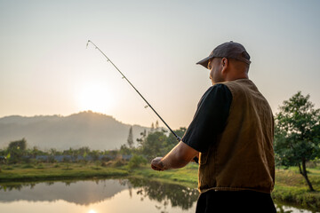 Excited emotion of Handsome fisherman fishing as a leisure activity during his vacation at the lake on sunset. Relax and hobby concept. - obrazy, fototapety, plakaty