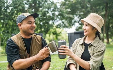 Young asian couple man and woman drinking coffee sitting in campsite outdoor. Two people camping in forest with coffee maker tools. Travel relax camping on vacation holiday weekend theme
