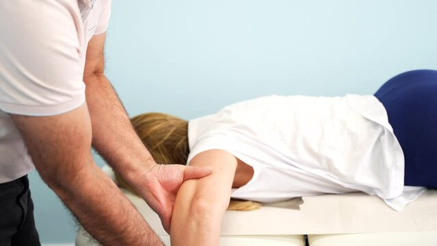 Physiotherapist correcting arm of woman on massage table. Closeup, zoom-out