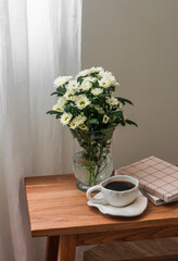 A cup of coffee, a bouquet of chrysanthemums, notepad, books on a wooden bench in the living room