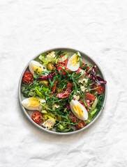 Healthy salad with vegetables, lightly salted salmon, olives, mozzarella, boiled eggs on a light background, top view
