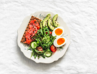 Delicious breakfast - salmon rye cracker sandwich, boiled egg, salad, avocado on a light background, top view