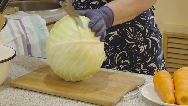Woman's hands cut a head of cabbage into pieces for shredding into strips. Close-up