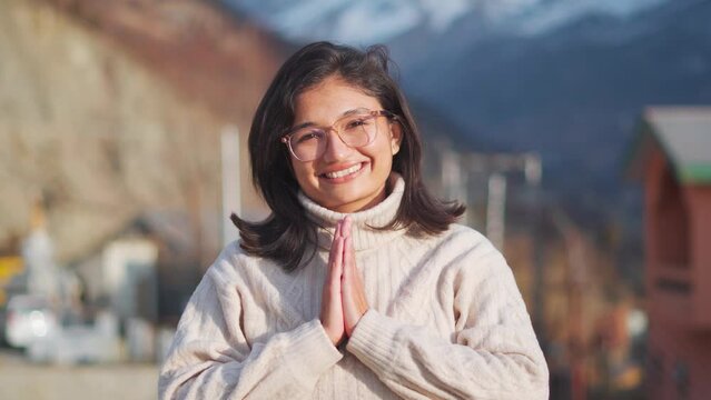 4K shot of Happy young girl showing namaste gesture by looking camera while standing in mountains at Keylong, Lahaul, India. Concept of welcome, greetings and Indian culture. Indian girl portrait.