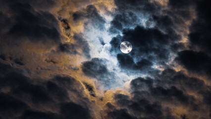 A picture capturing the moon veiled by thick clouds, emitting a soft glow that creates a serene and...
