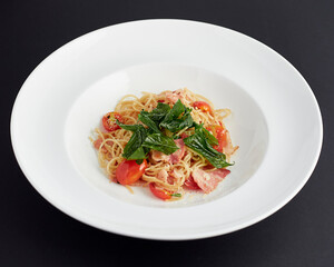 Spaghetti with ham, tomatoes and cheese served in white plate isolated on black background. italian food.