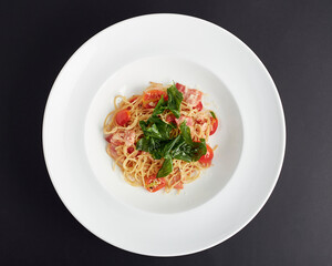 Top view of Spaghetti with ham, tomatoes and cheese served in white plate isolated on black background. italian food.