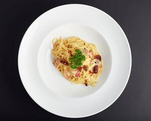 Top view of Spaghetti Carbonara topped with ham, bacon, sliced mushroom and rosemary leaves served in white plate isolated on black background. italian food.