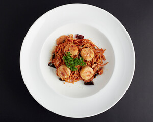 Top view of Stir-Fried Spaghetti With Dried Chili and scallop served in white plate isolated on black background. italian food. Spicy taste from dried chilies.