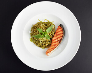Top view of spaghetti pesto sauce with salmon served in white plate isolated on black background. italian food.