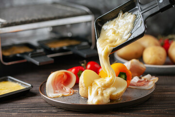 Delicious traditional Swiss melted raclette cheese on diced boiled or baked vegetables served in...