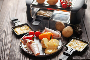 Delicious traditional Swiss melted raclette cheese on diced boiled or baked vegetables served in...