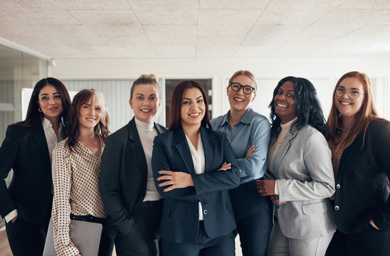Smiling group of diverse businesswoman standing together in a boardroom. They are all wearing suits in different colors
