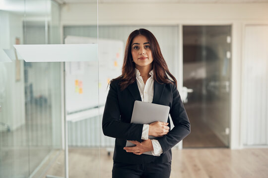 Confident businesswoman standing with a laptop at the entrance to a boardroom