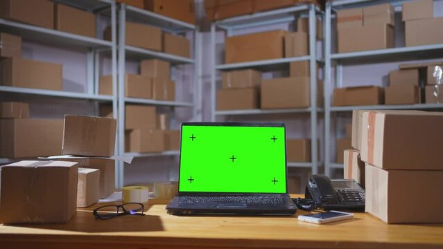 laptop with a green screen on the background of a warehouse with parcels in boxes ,no body