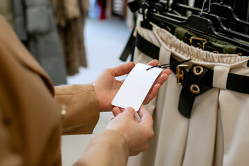 Woman is shopping for casual clothes, female's hands holding price tag mockup in clothing store, in boutique trying on clothes differents blouses quality of fabric. Shopping in Clothing Store.	