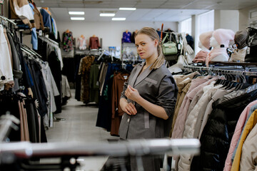 Fototapeta na wymiar Woman is shopping for casual clothes, grey costume fashionable women's clothing store, in boutique inspecting differents blouses price tags and the quality of fabric. Shopping in Clothing Store. 