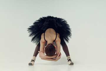 ballerina in a black tutu is leaning forward with her arms crossed behind her back