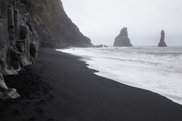 icelandic black beach, reynisfjara beach, rocks sticking out of the water, basalt cliffs,...