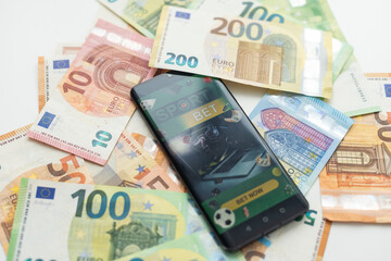 Smartphone with gambling mobile application with money close-up. Sport and betting concept - obrazy, fototapety, plakaty
