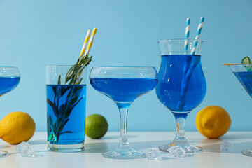 Blue drink in cocktail glasses, lemons, limes and ice cubes on blue background