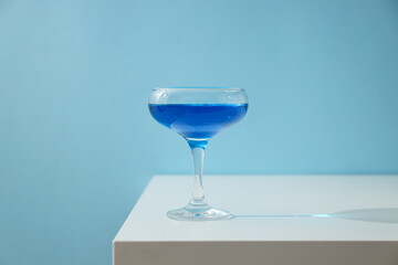 Blue drink in cocktail glass on blue background, close up