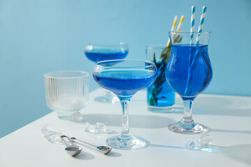 Blue drink in cocktail glasses and ice cubes on blue background, close up