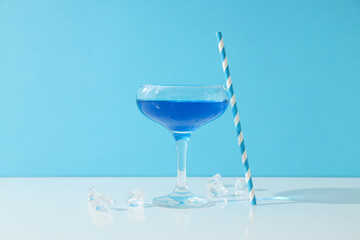 Blue cocktail in glass, straw and ice cubes on blue background