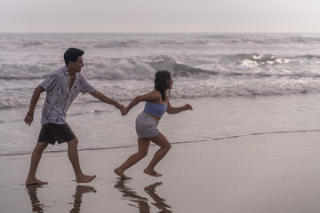 Couple running hand in hand along the seashore in the afternoon