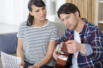 happy couple playing guitar while sitting on sofa