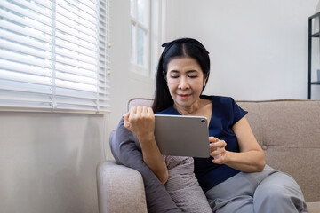 Elderly woman's leisure day watching social media on tablet, watching news on sofa in living room