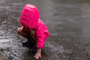 An Asian little girl wearing a pink jacket and playing in the rain on the asphalt road