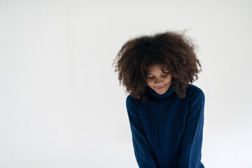 A young woman with a gentle smile, curly hair, wearing a blue sweater, in a bright minimalist...