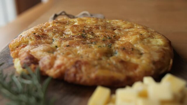 potato and cheese omlete, wide pan, decorated rustic wooden plate with rosemary