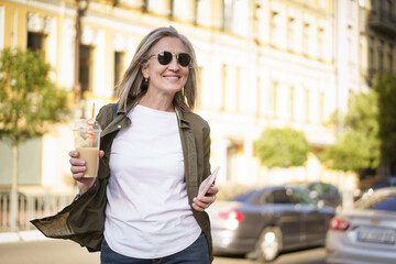 A woman strolling along a busy street while carrying a beverage in her hand.